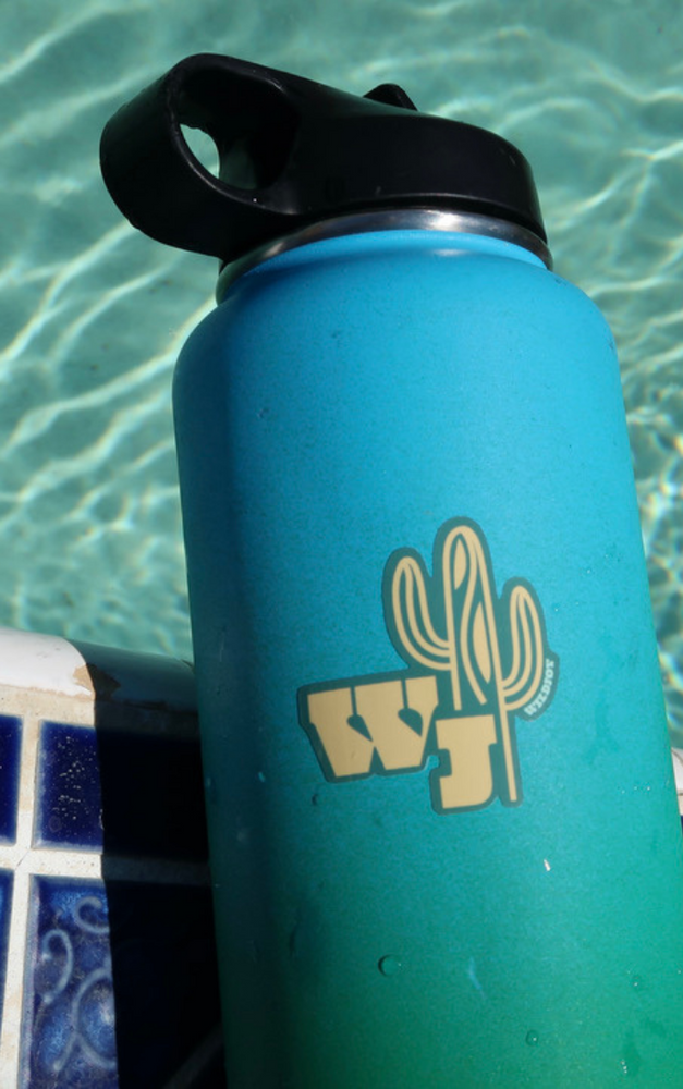 WJ Saguaro Sticker in teal with yellow lettering in addition to the wildjoy lettered on the arm of the saguaro. It is on a teal waterbottle with a black lid. It's resting on the ledge on the wall dangling over the pool.